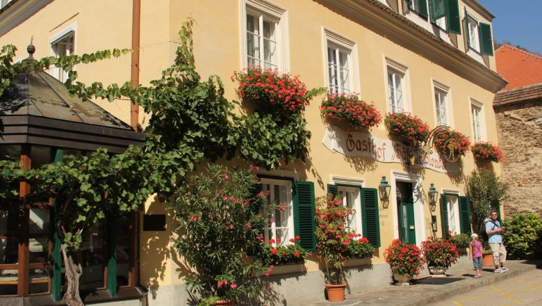 Hotel, © Schendl Ein traditionelles Gasthaus mit gelber Fassade, grünen Fensterläden und blühenden Blumenkästen.