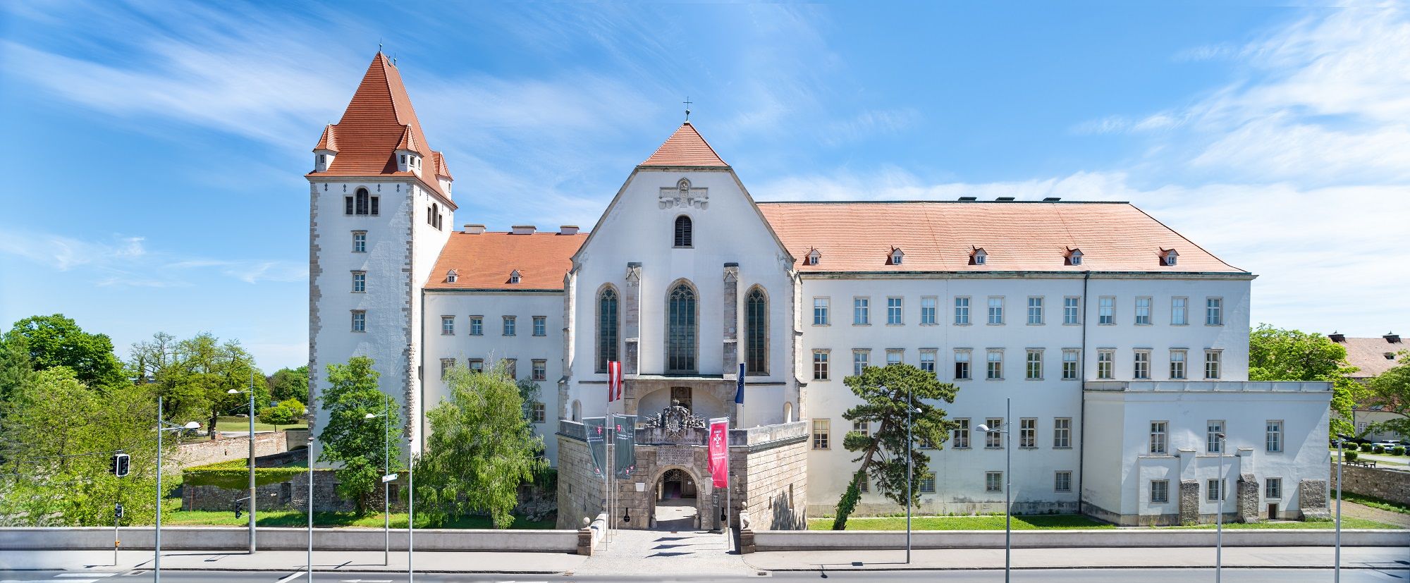 Panoramablick auf die Burg Wiener Neustadt mit rotem Dach und blauem Himmel.