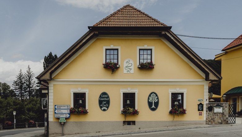 Gelbes Gasthaus mit Blumenk&auml;sten und Schildern an der Fassade.