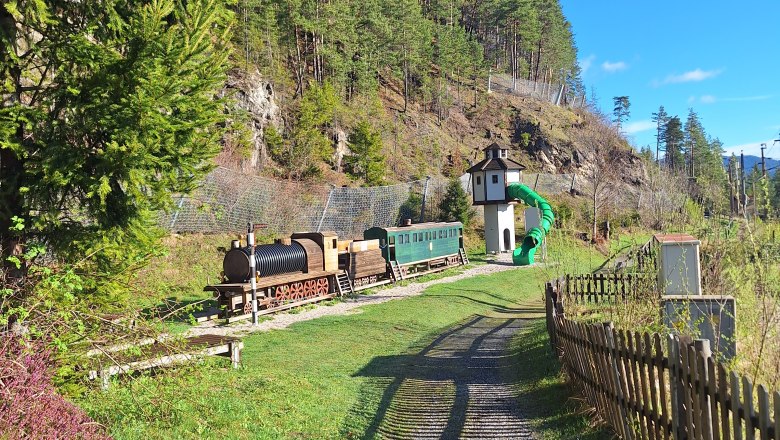 Kinderspielplatz mit einer Holzlokomotive und einem Rutschenturm.