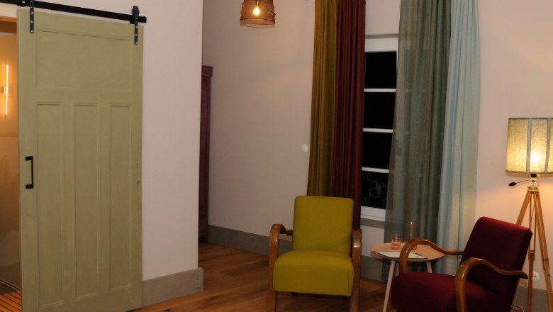 Gem&uuml;tliches Zimmer mit zwei Sesseln, Vorh&auml;ngen und Stehlampe.