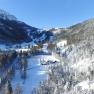 Winterlandschaft mit verschneiten Bergen und einem Hof im Tal.
