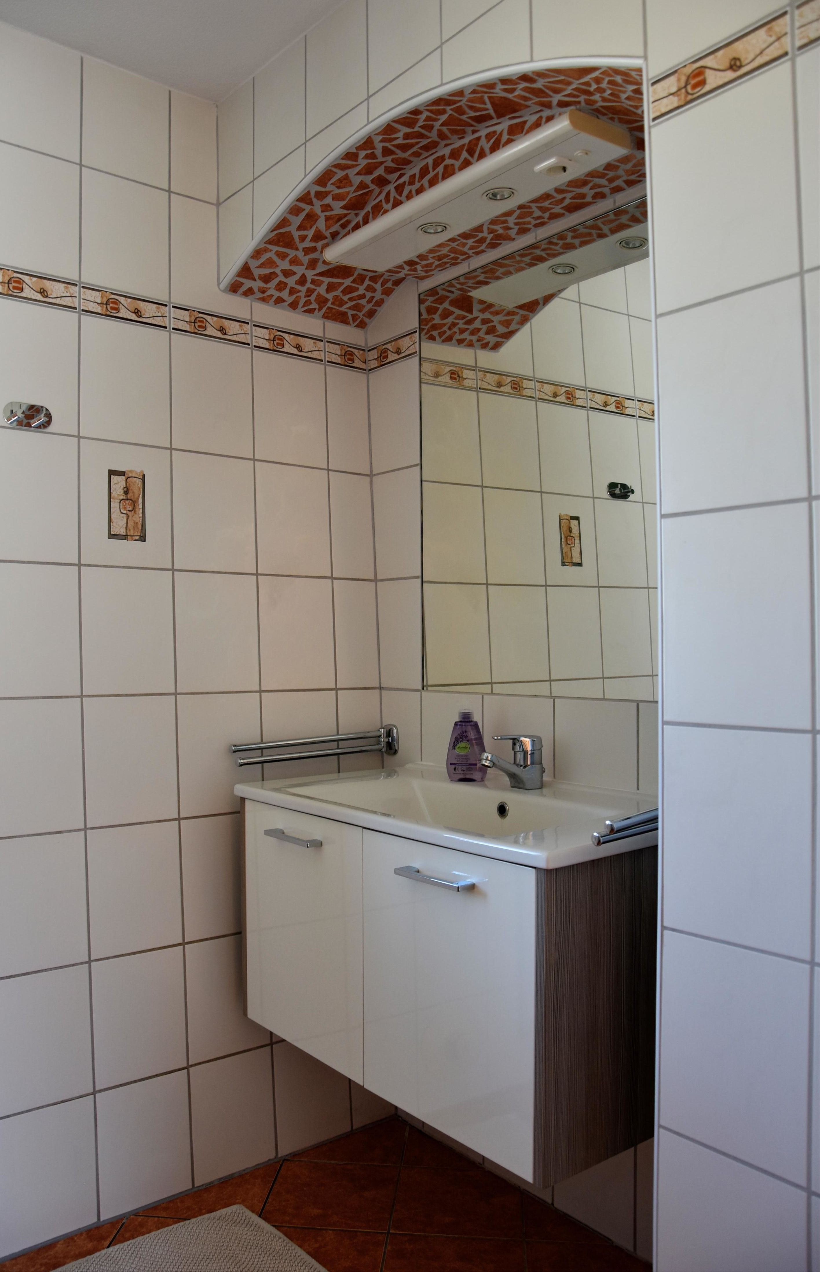 Badezimmer mit Spiegel, Waschbeckenunterschrank, Dusche und dekorativer Deckenverkleidung.