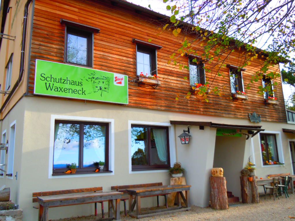 Eingang zum Schutzhaus Waxeneck mit Holztischen und Blumenkästen.