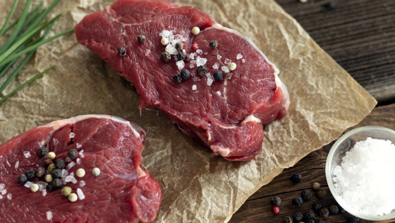 Zwei St&uuml;ck rohes Rindfleisch mit Salz und Pfeffer bestreut auf Backpapier, daneben Schnittlauch, eine Schale Salz und Pfeffer.