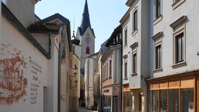 Schmale Gasse mit alten Geb&auml;uden und Kirchturm im Hintergrund.