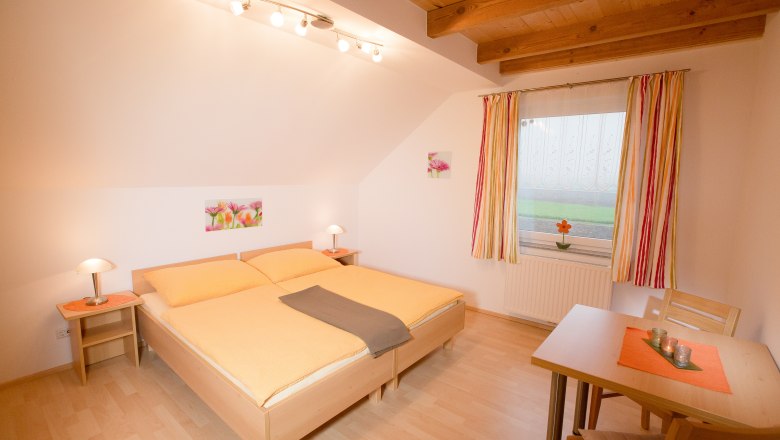 Gem&uuml;tliches Schlafzimmer mit Doppelbett, Holzbalkendecke und Tisch mit St&uuml;hlen.