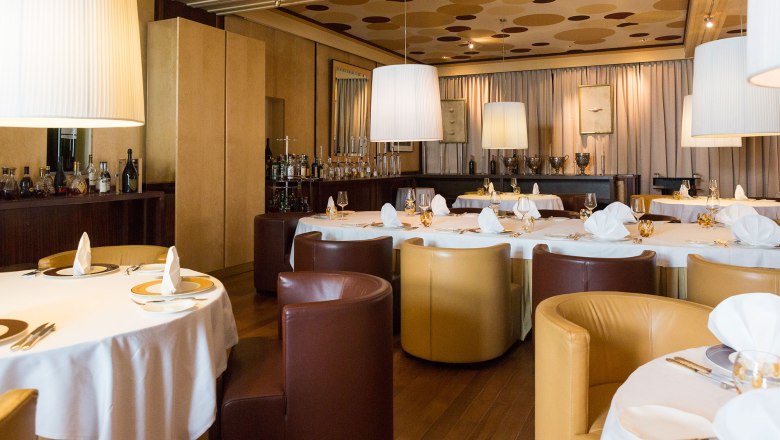 Eleganter Speisesaal mit runden Tischen, wei&szlig;en Tischdecken und braunen sowie beigen Sesseln.