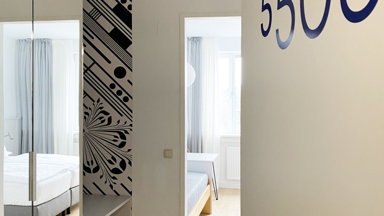 Blick in ein G&auml;stezimmer mit der Nummer 5505, modern eingerichtet mit Bett und Spiegel.