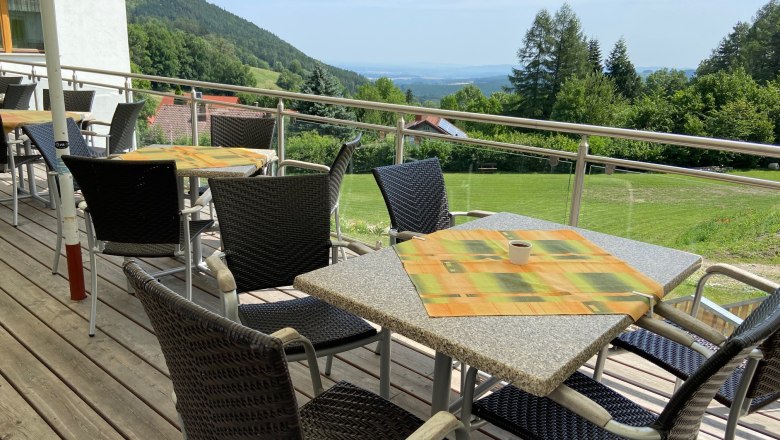 Terrasse mit Tischen und St&uuml;hlen, Blick auf gr&uuml;ne H&uuml;gel und B&auml;ume im Hintergrund.