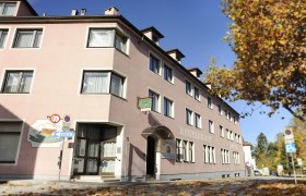 Außenansicht des Hotels Osterbauer mit rosa Fassade und Herbstlaub auf dem Boden.