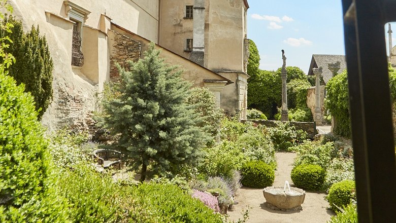 Ein gepflegter Garten mit B&uuml;schen und einem kleinen Brunnen vor einem historischen Geb&auml;ude.