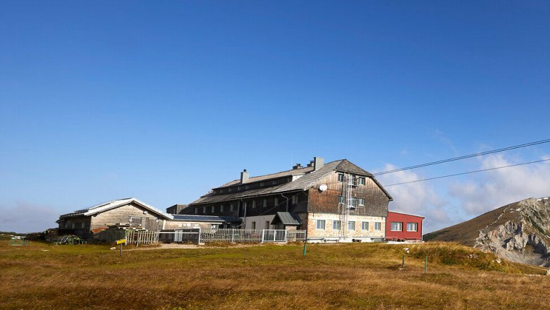 Panoramablick auf einen Bergh&uuml;tte mit umliegenden Gipfeln unter blauem Himmel.