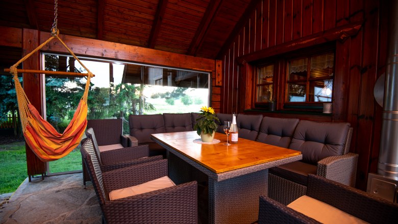 &Uuml;berdachte Terrasse mit Holztisch, Rattanm&ouml;beln und H&auml;ngesessel.