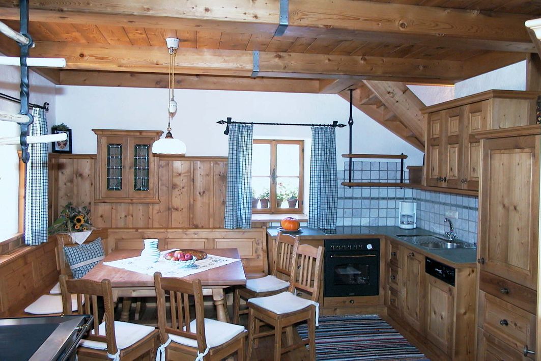 Rustikale Küche mit Holzmöbeln, Esstisch und Stühlen, Herd, Spüle und Fenster mit karierten Vorhängen.