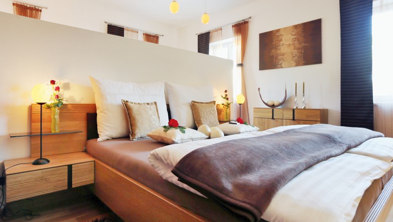 Gem&uuml;tliches Schlafzimmer mit Doppelbett, dekoriert mit Kissen und Rosen, Holzm&ouml;beln und sanfter Beleuchtung.