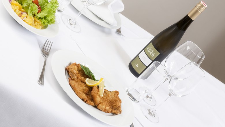 Landgasthof Mann Königsbrunn Speisen, © Landgasthof Mann Königsbrunn Gedeckter Tisch mit Schnitzel, Salat und Weinflasche.
