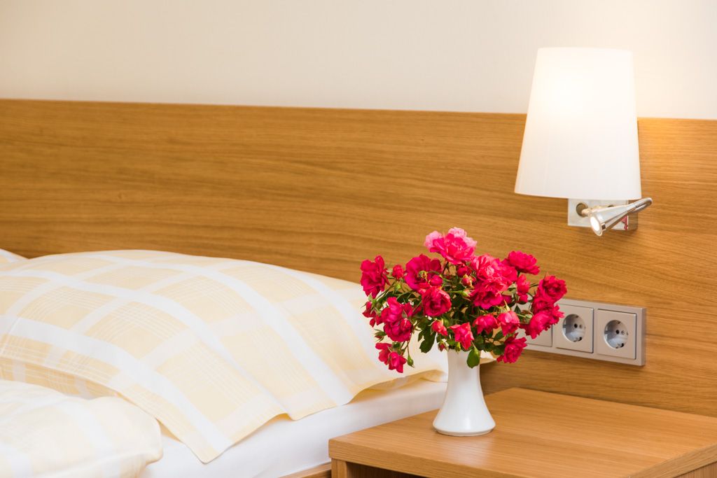 Ein Gästezimmer mit einem Bett, einer Nachttischlampe und einem Blumenstrauß in einer Vase auf dem Nachttisch.