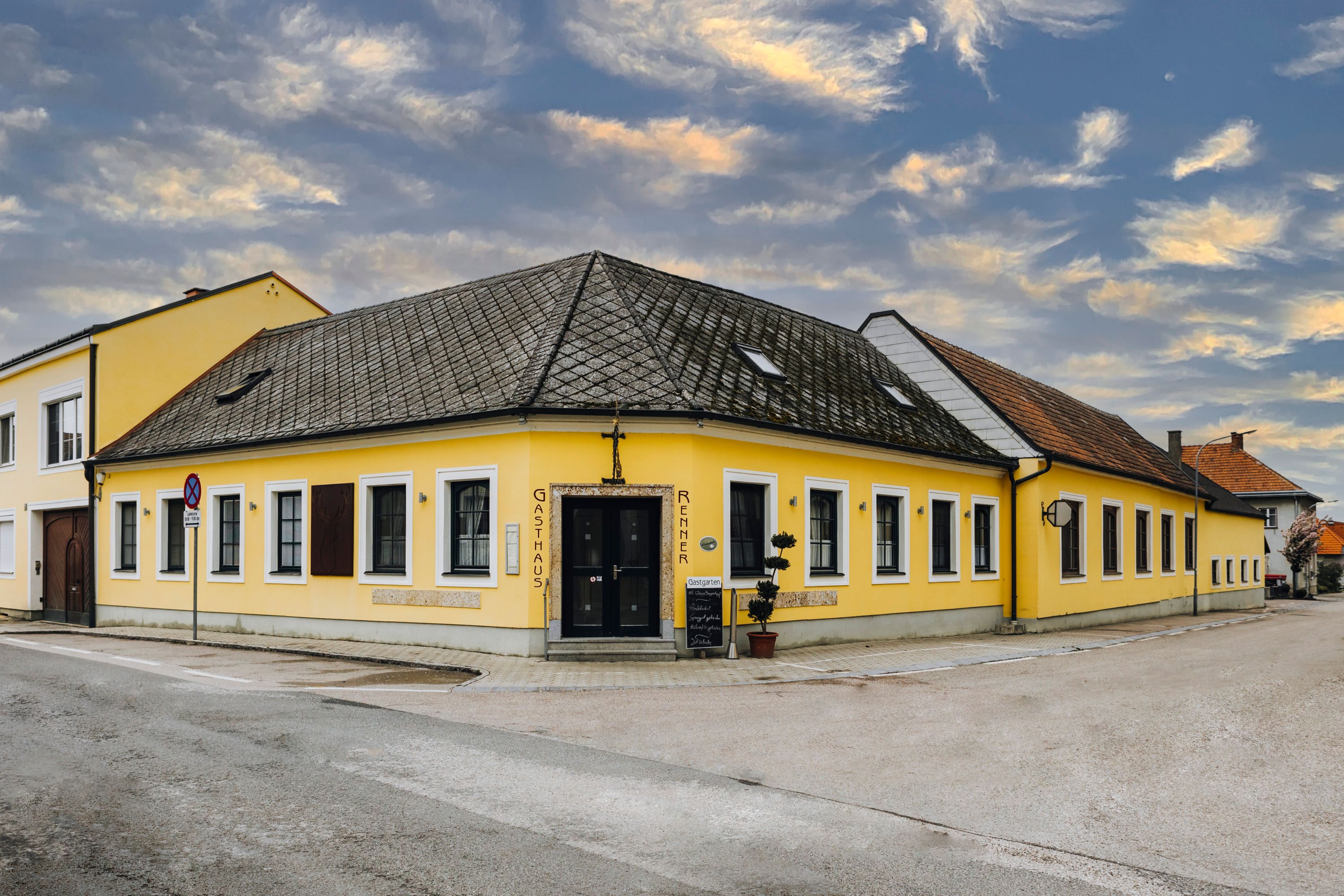 Gelbes Gasthaus an Straßenecke mit bewölktem Himmel im Hintergrund.