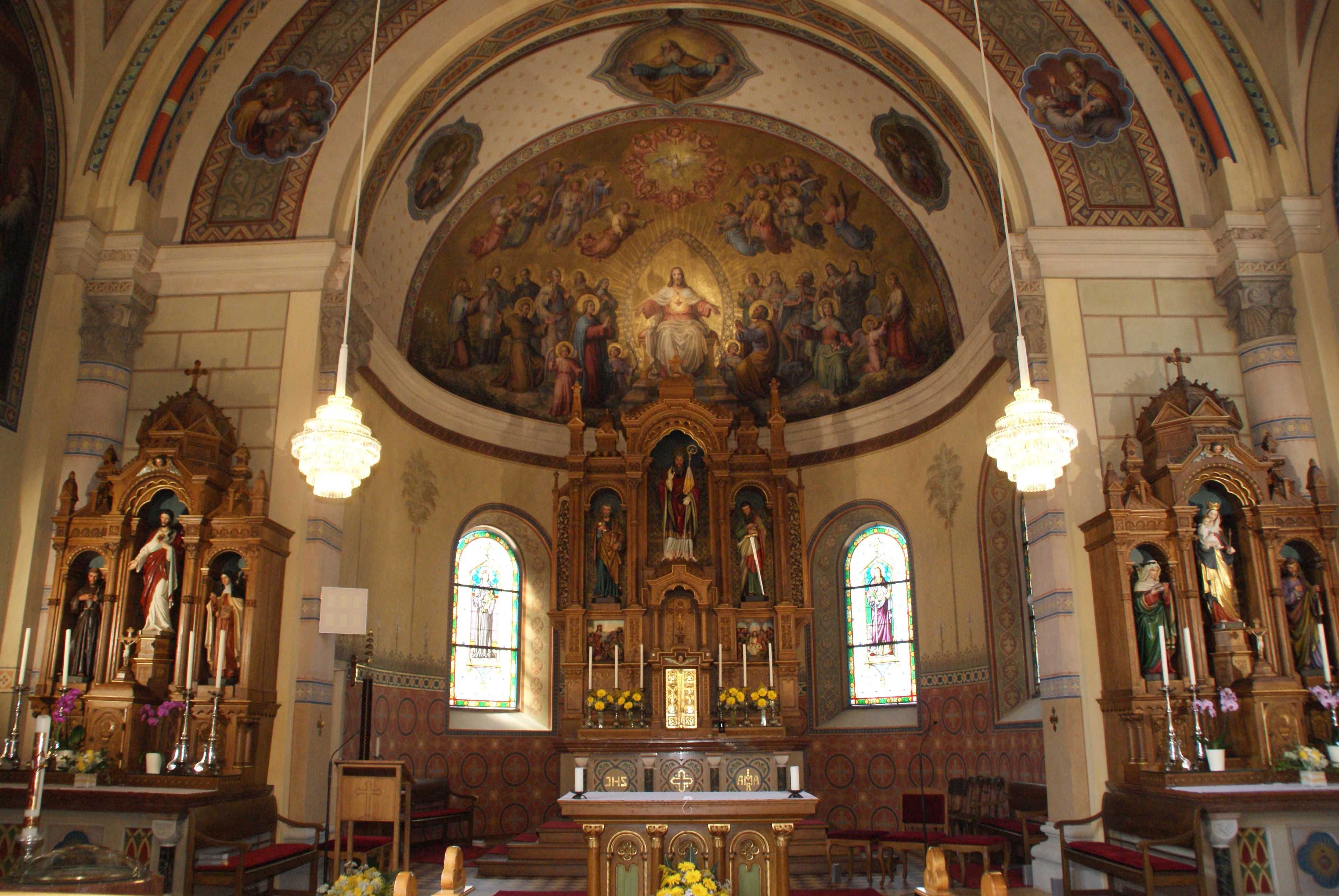 Innenansicht einer reich verzierten Kirche mit Altar, Heiligenstatuen und Wandmalereien.