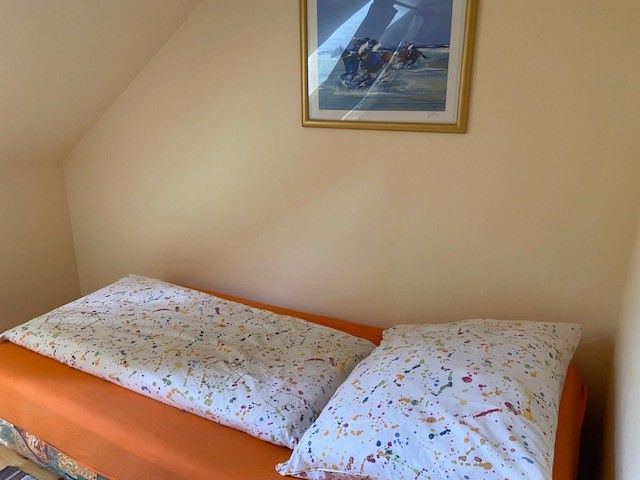 Ein Bett mit bunter Bettwäsche in einem Einzelzimmer, darüber ein gerahmtes Bild an der Wand.