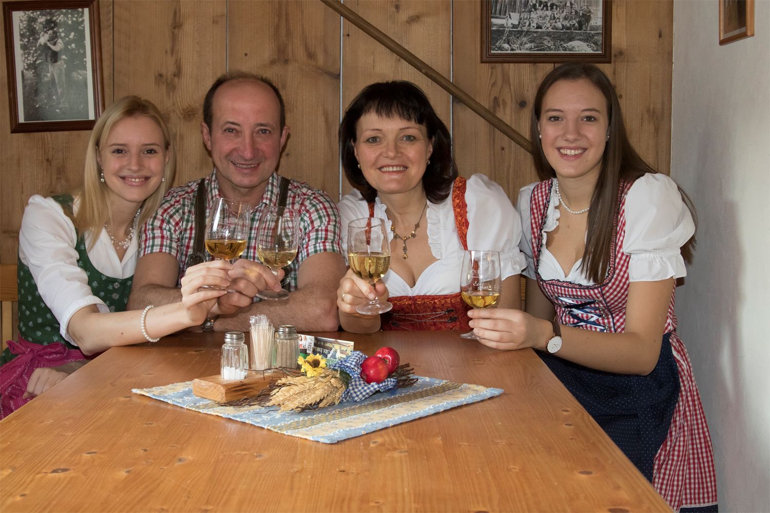 Eine Familie in traditioneller Kleidung stößt mit Weingläsern an einem Holztisch an.