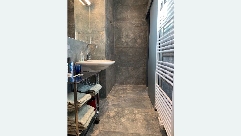 Modernes Badezimmer mit grauen Fliesen, Waschbecken, Handtuchregal und Heizkörper.