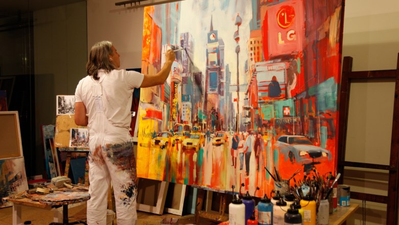 Ein Künstler malt ein lebhaftes Stadtbild auf einer großen Leinwand in einem Atelier.