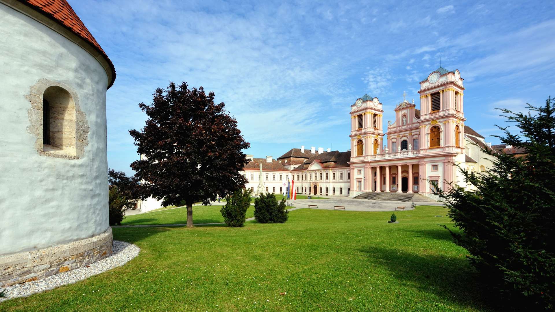 Innenhof des Stifts Göttweig mit grüner Wiese, Bäumen und barocker Architektur im Hintergrund.