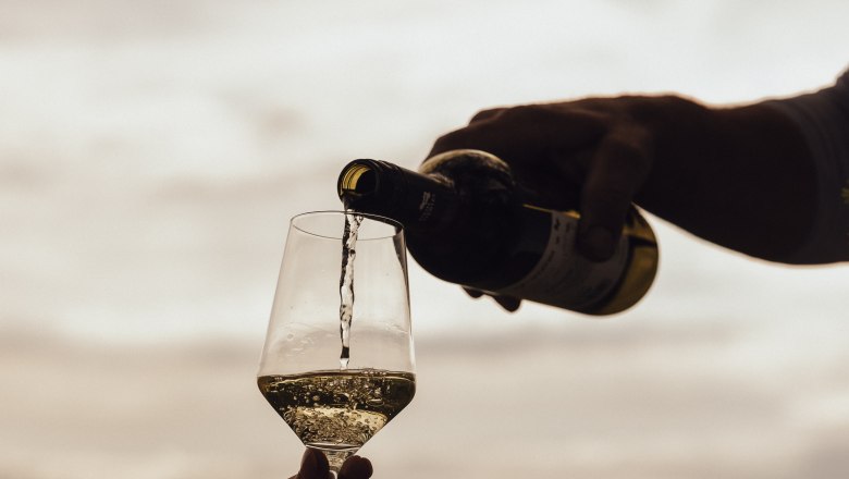 Wein wird in ein Glas im Freien eingeschenkt, mit einem verschwommenen Hintergrund von Weinbergen.