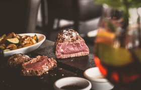 Ein saftiges Steak auf einem hei&szlig;en Stein, begleitet von Gem&uuml;se und So&szlig;en in Sch&auml;lchen.
