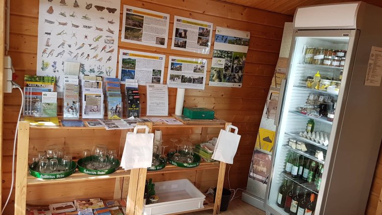 Innenansicht eines kleinen Verkaufsstands mit Infomaterial und K&uuml;hlschrank.