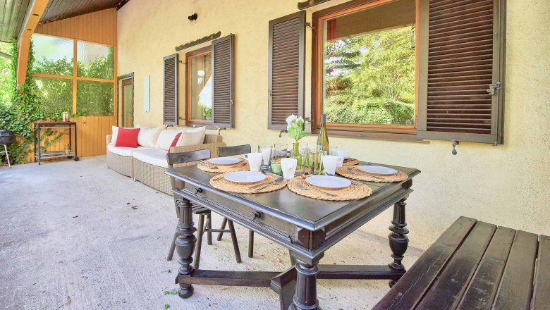 Terrasse mit Esstisch, Stühlen und Sofa, umgeben von Pflanzen.