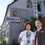 Ein Mann und eine Frau stehen vor einem Gebäude mit der Aufschrift 'Hotel Burger'.