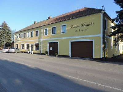Gelbes Gebäude mit der Aufschrift 'Pension Daniela' an einer Straße.