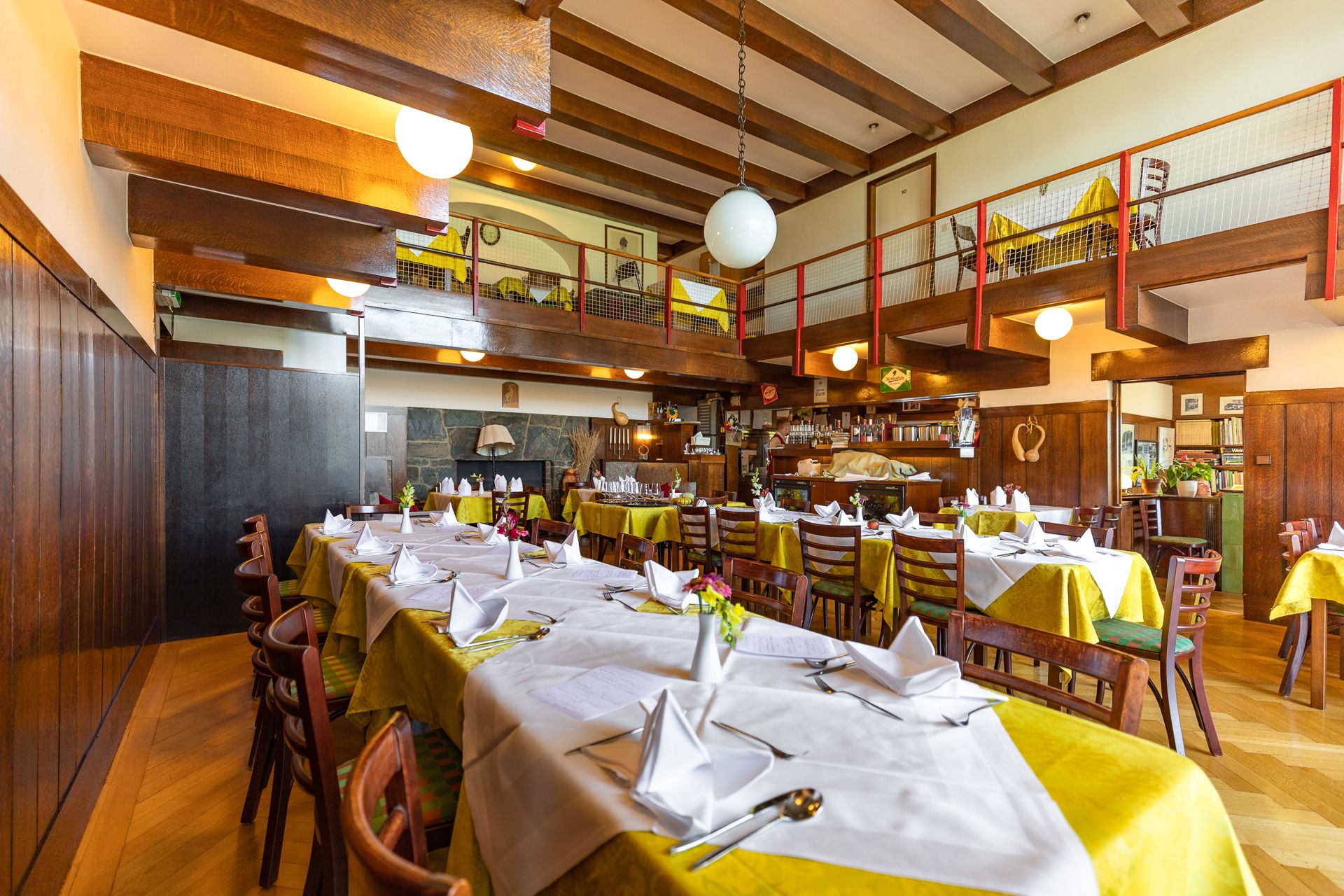 Innenansicht eines gemütlichen Restaurants mit Holzbalken, gedeckten Tischen und einer Galerie.