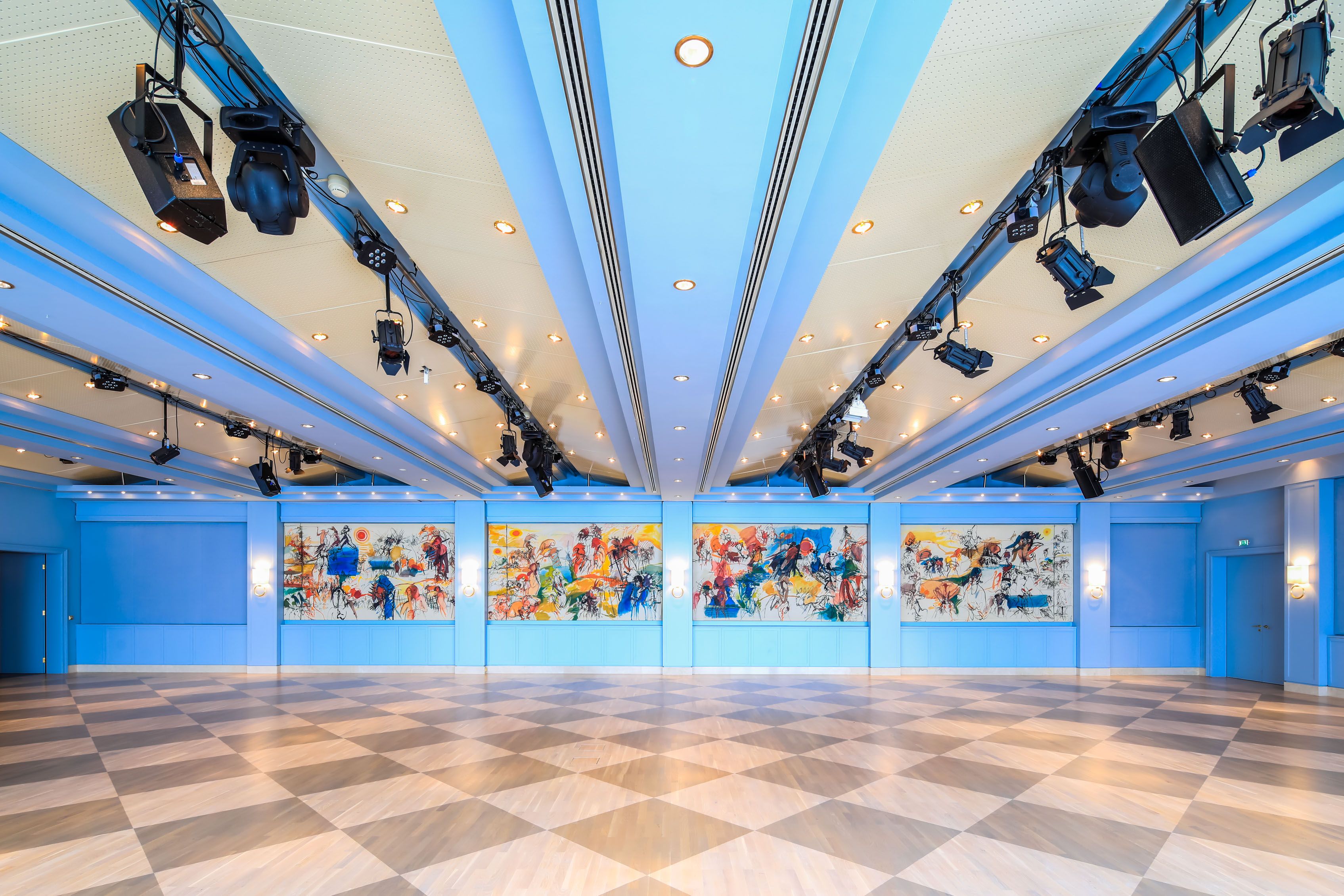 Innenansicht des Badener Saals im Congress Center Baden mit blauer Decke, bunten Wandgemälden und diagonalen Bodenfliesen.