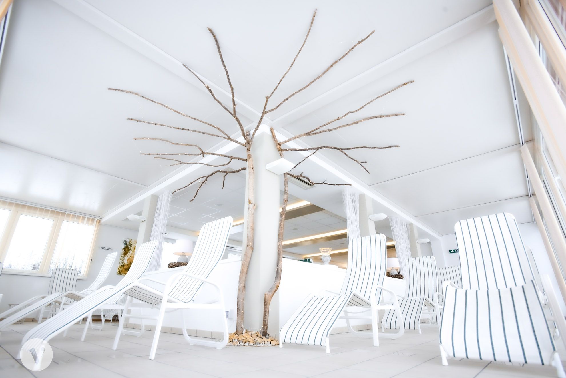 Ein heller Ruhebereich mit weißen Liegestühlen und einem dekorativen Baumstamm in der Mitte.