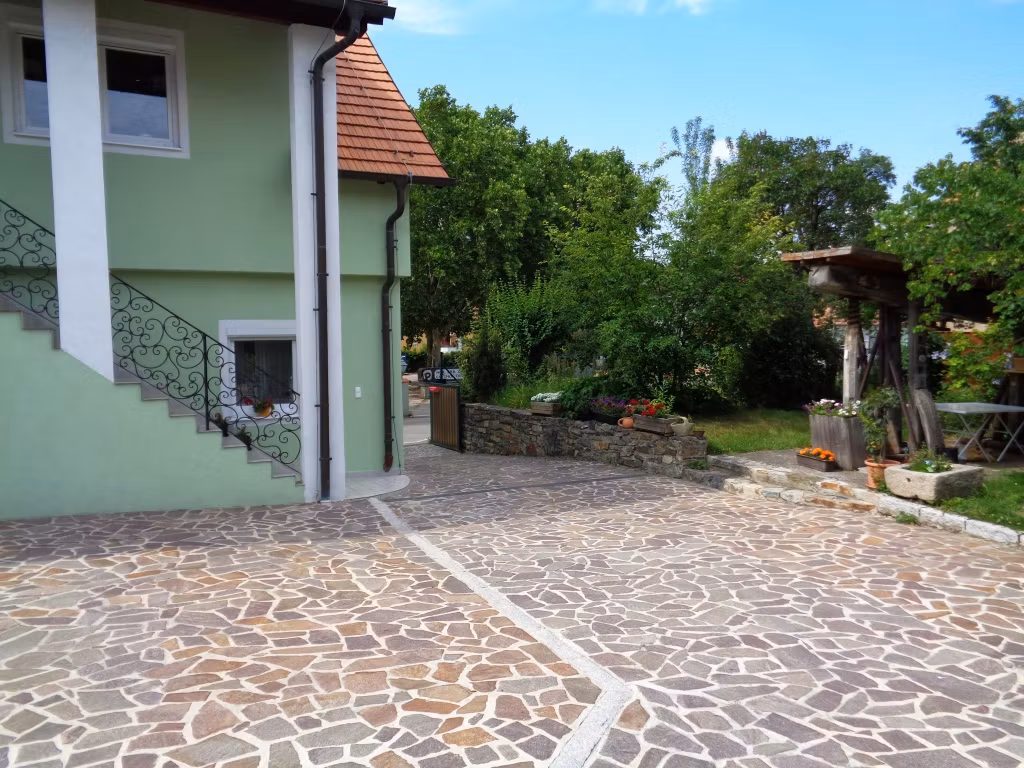 Innenhof mit gepflastertem Boden, grünem Haus und Garten.