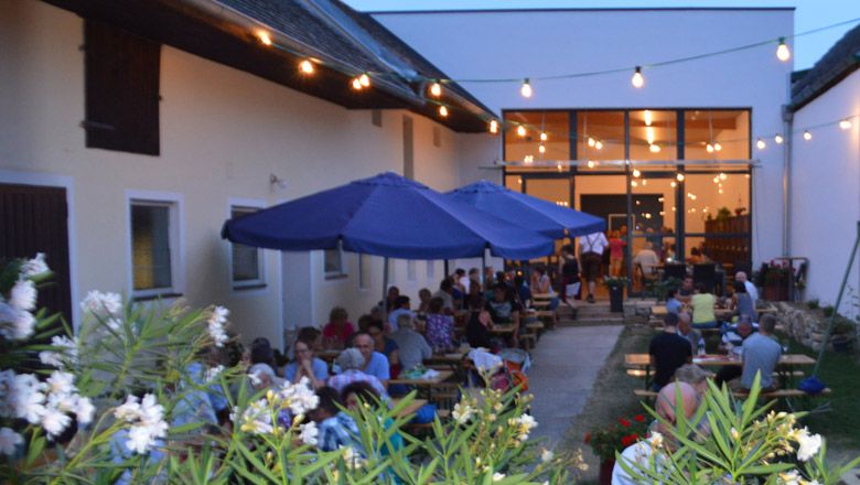 Heurigenlokal mit Gästen im Freien, beleuchtet von Lichterketten.