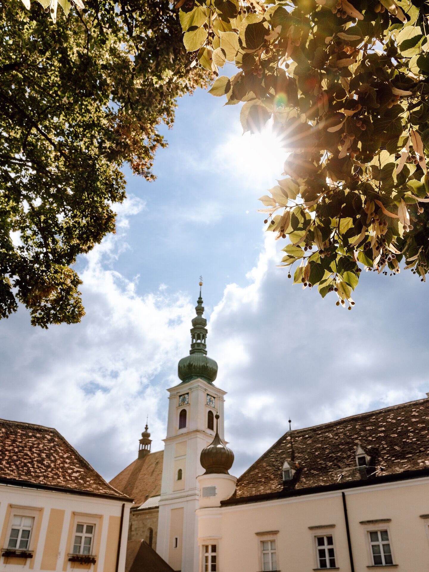Die sanften Strahlen der Sonne brechen durch das Blätterdach und tauchen die historische Architektur in ein warmes Licht. Umgeben von üppigem Grün und dem beruhigenden Klang der Natur, lädt dieser Ort zur Besinnung und Erholung ein. Hier, wo Geschichte und Natur harmonisch verschmelzen, wird der Sommer zu einem unvergesslichen Erlebnis.