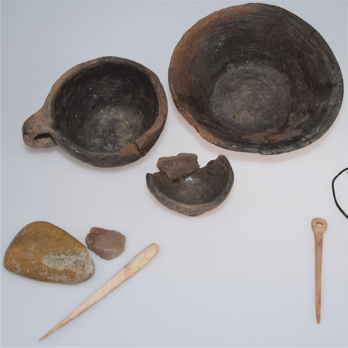 Prähistorische Artefakte wie Schalen, Werkzeuge und Steine auf weißem Hintergrund.
