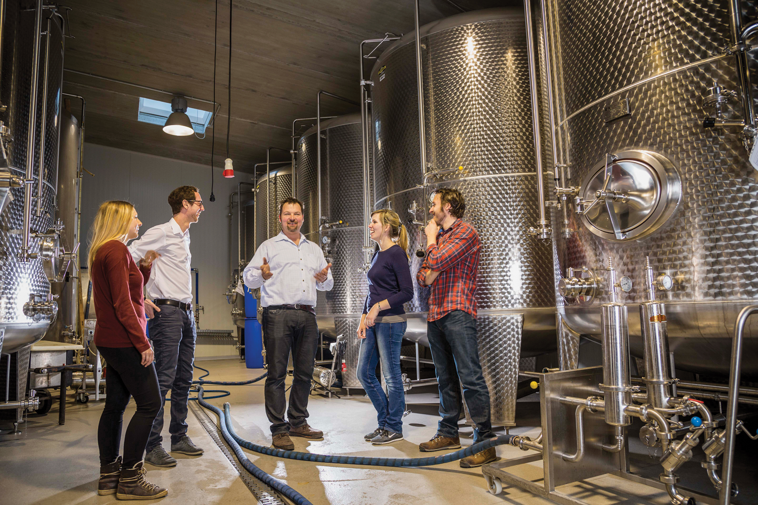 Gruppe von Menschen in einer Brauerei mit großen Metalltanks.