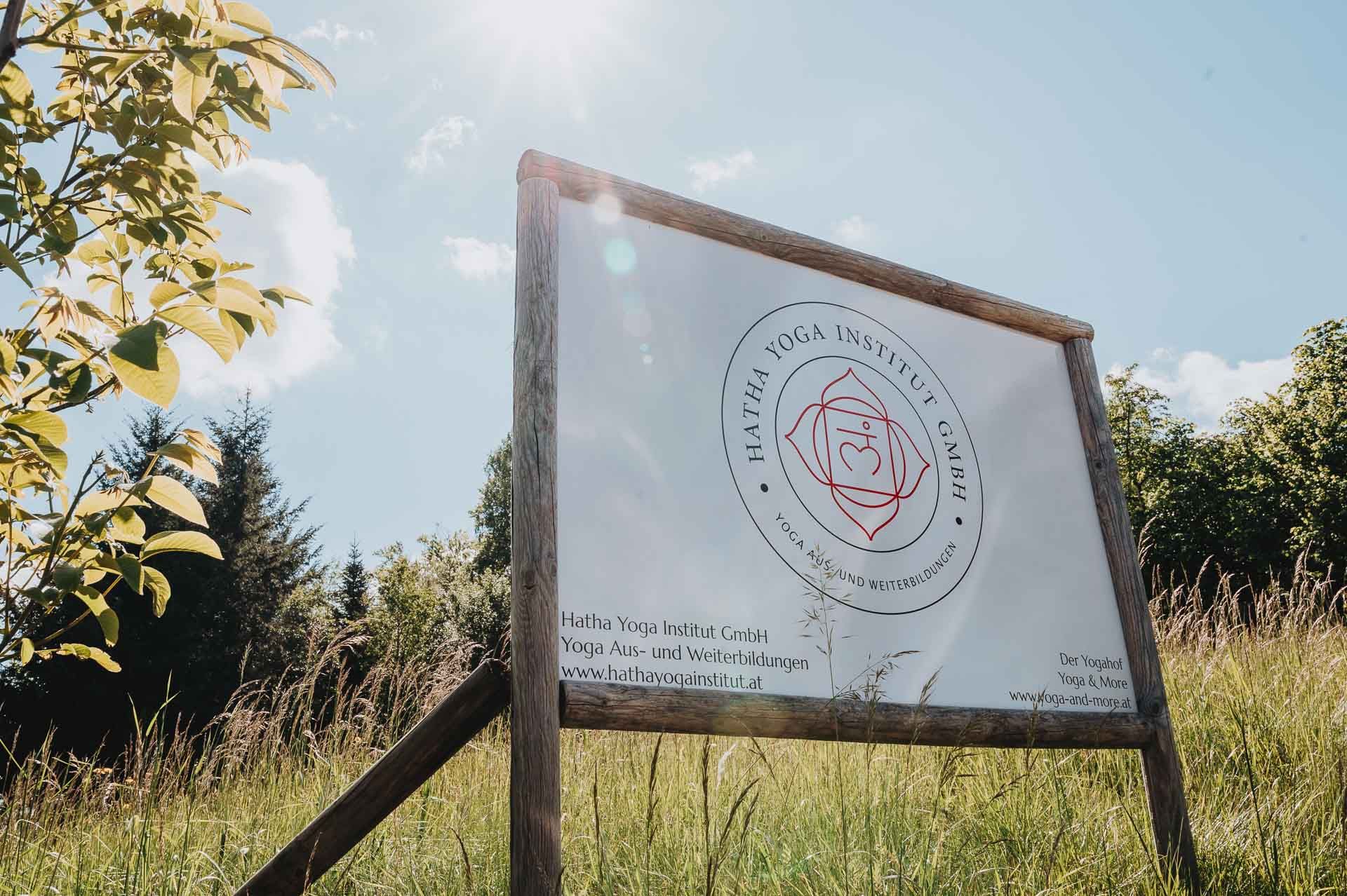 Ein Schild des Hatha Yoga Instituts steht auf einer Wiese unter einem sonnigen Himmel.