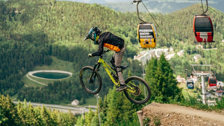 Mountainbiker springt im Bikepark Semmering, im Hintergrund Seilbahn und Wald.