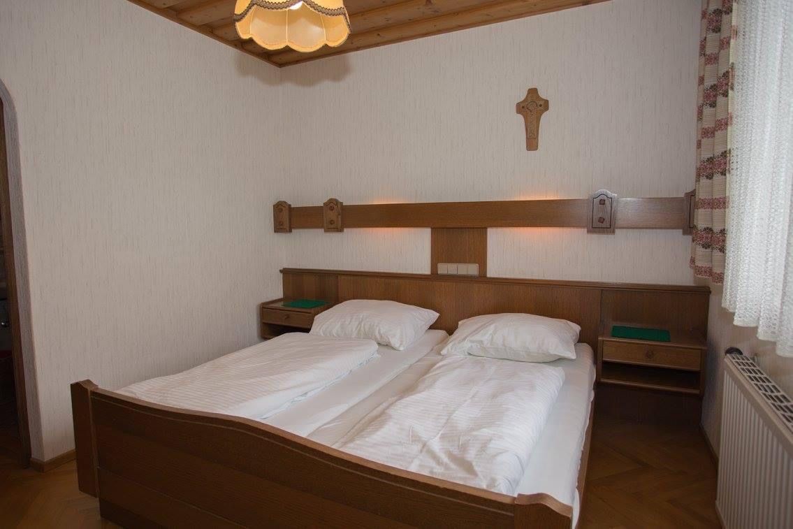 Ein traditionelles Doppelzimmer mit Holzmöbeln, zwei Betten, einem Kreuz an der Wand und einer Lampe an der Decke.