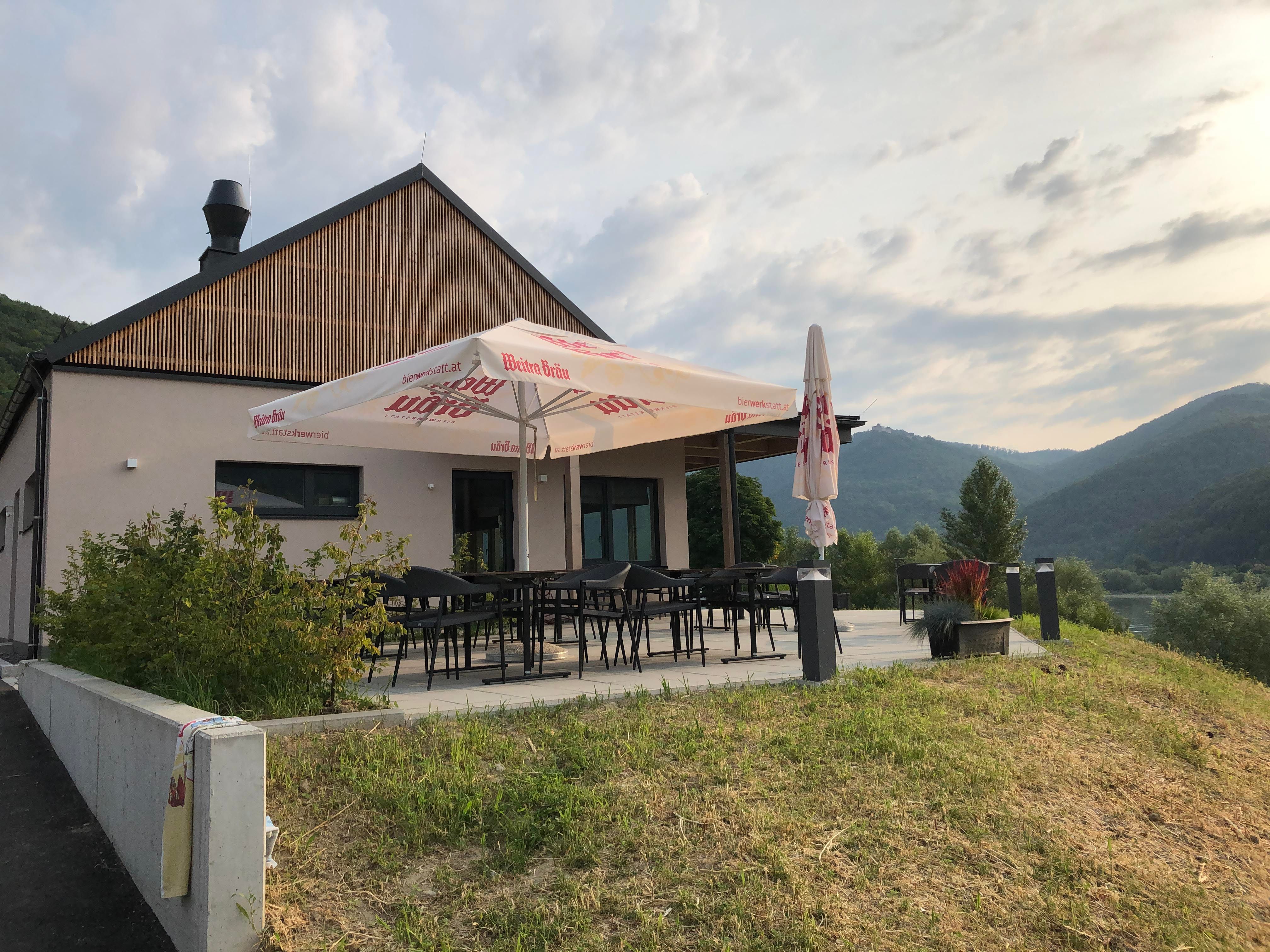 Moderne Terrasse mit Sonnenschirm, umgeben von grüner Landschaft und Hügeln.