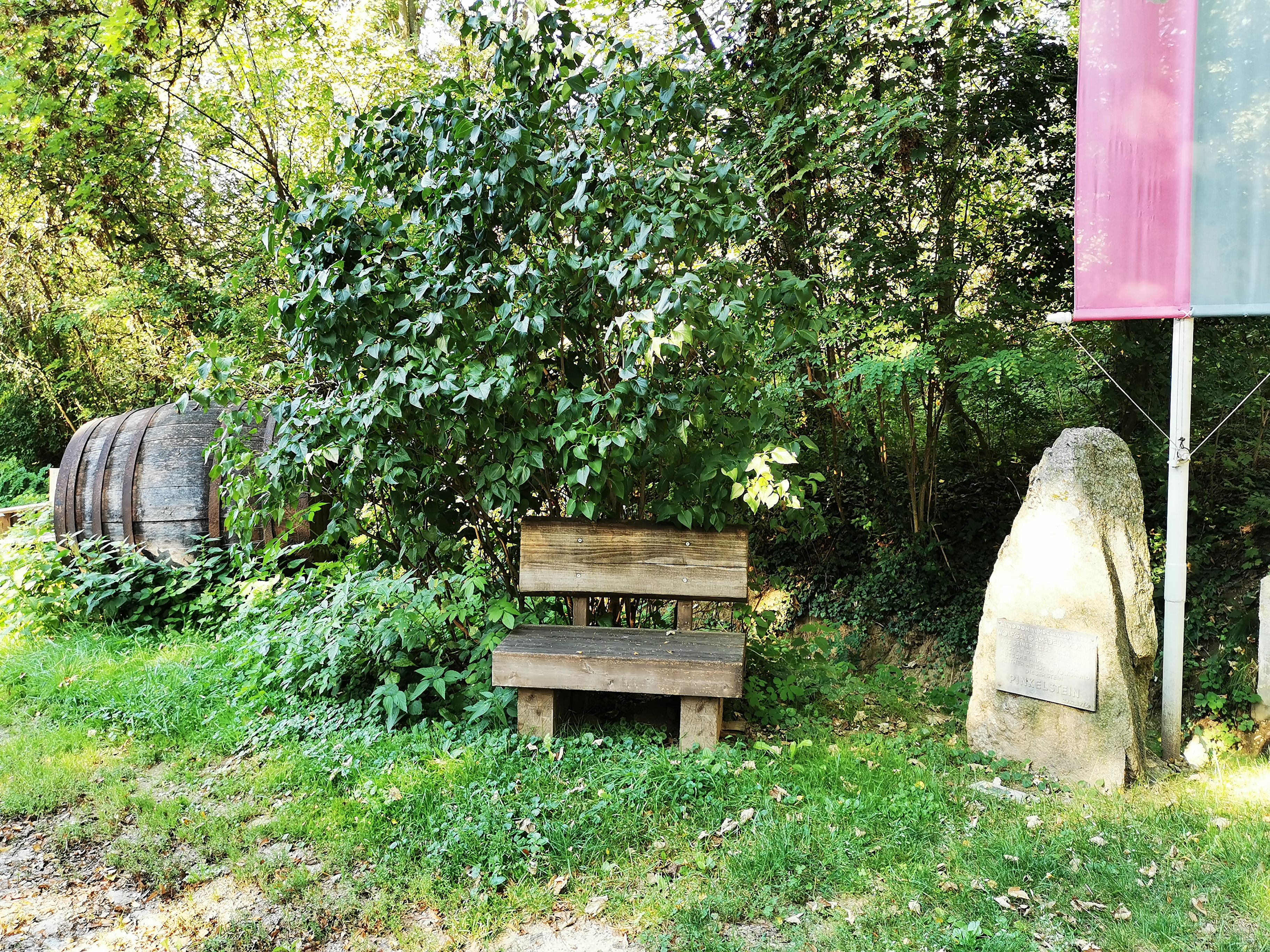 Holzbank neben einem Stein mit Inschrift im Grünen.