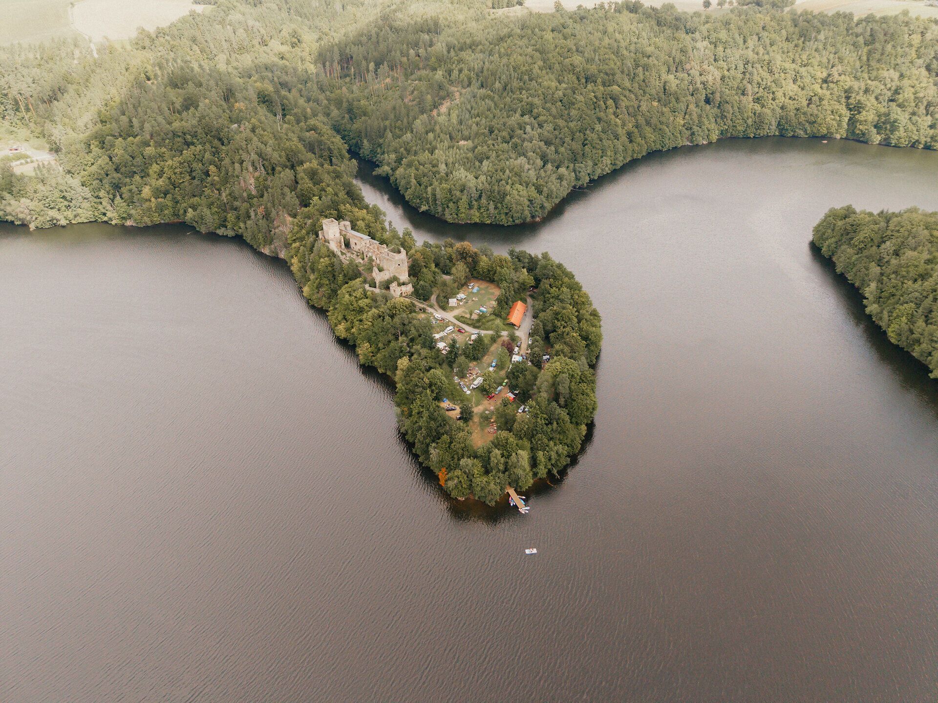 Drohnenaufnahme der bewaldeten Halbinsel mit der Ruine Dobra im Stausee Dobra; die Ruine liegt von Wasser umgeben, mit kleinen Booten und Wiesenflächen am Ufer.
