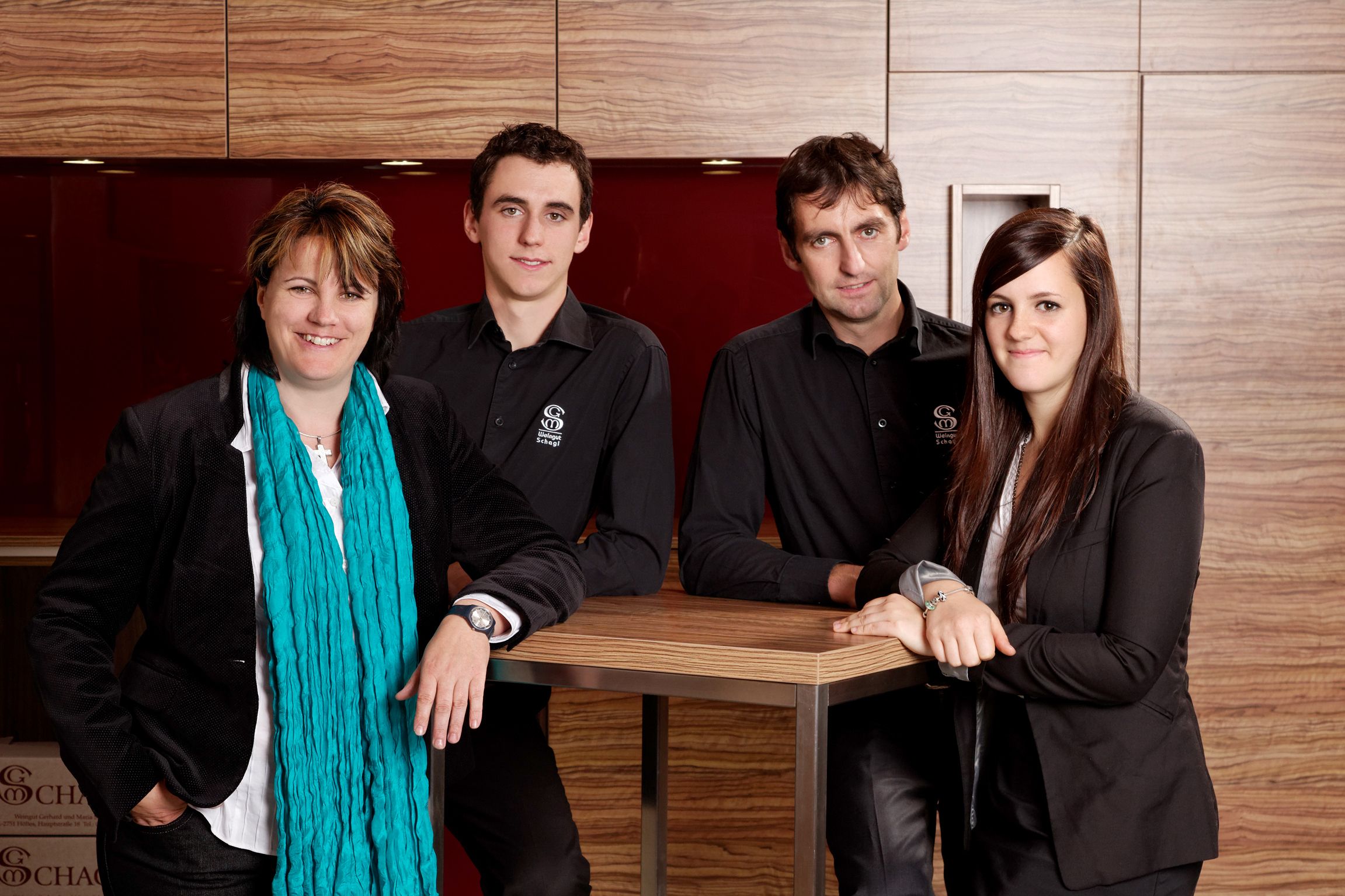 Vier Personen stehen lächelnd vor einer Holzwand.